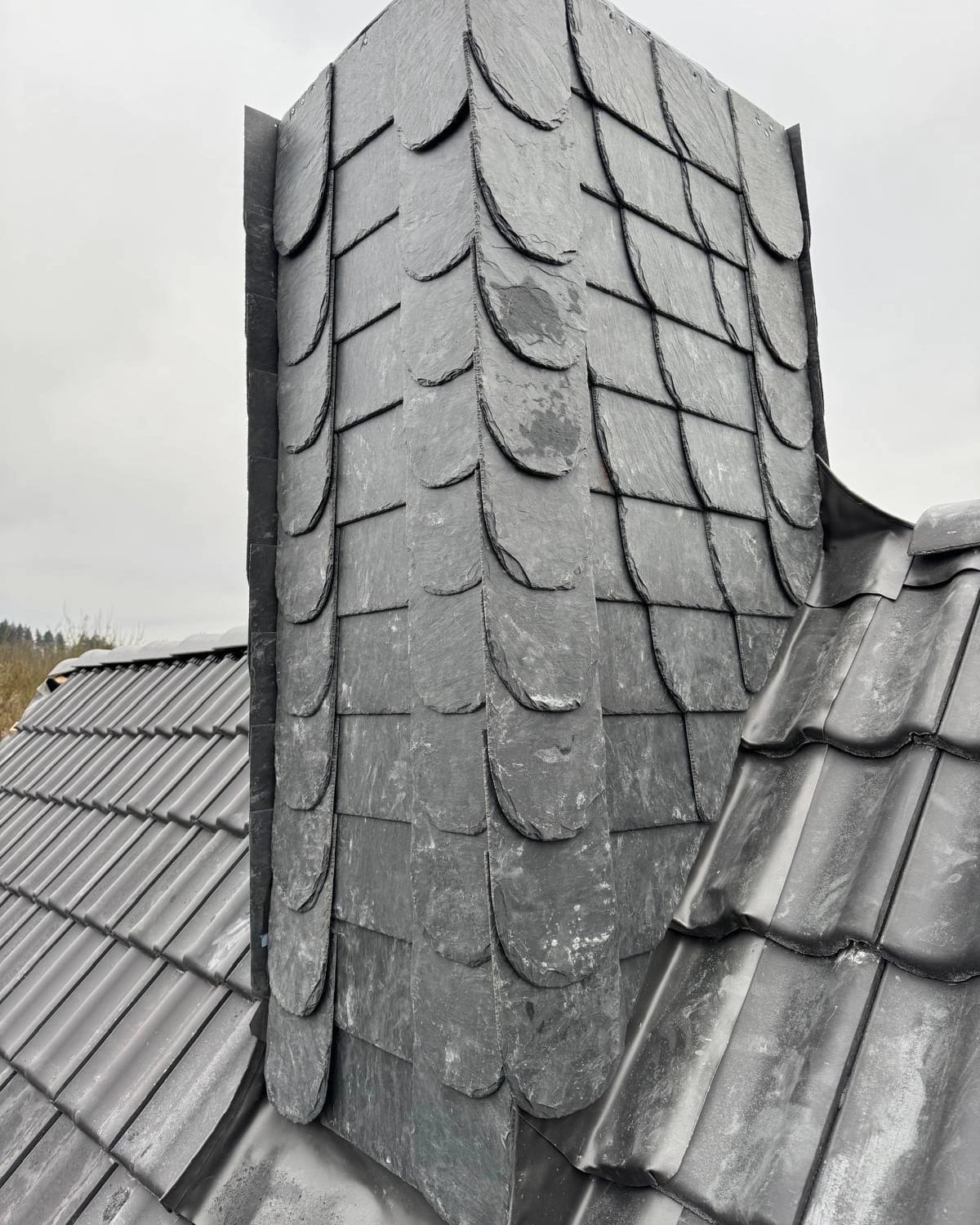 Mit Naturschiefer verkleideter Kamin auf einem grauen Ziegeldach